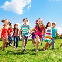 Dieses Bild zeigt eine Gruppe lachende Kinder, welche Hand in Hand über eine Wiese laufen.